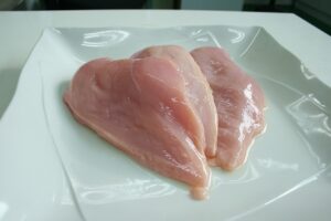 Pollo crudo su un tagliere, evidenziando il rischio batterico senza lavarlo prima della cottura.